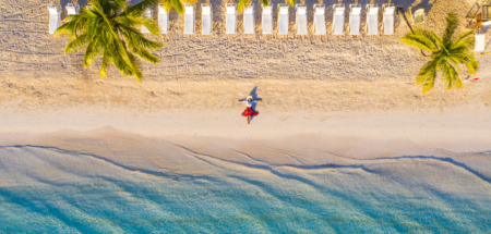 Vrouw in rode rok ligt op idyllisch tropisch strand onder palmbomen