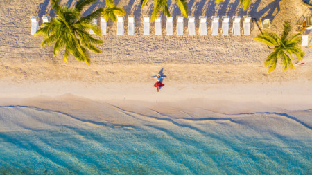 Vrouw in rode rok ligt op idyllisch tropisch strand onder palmbomen