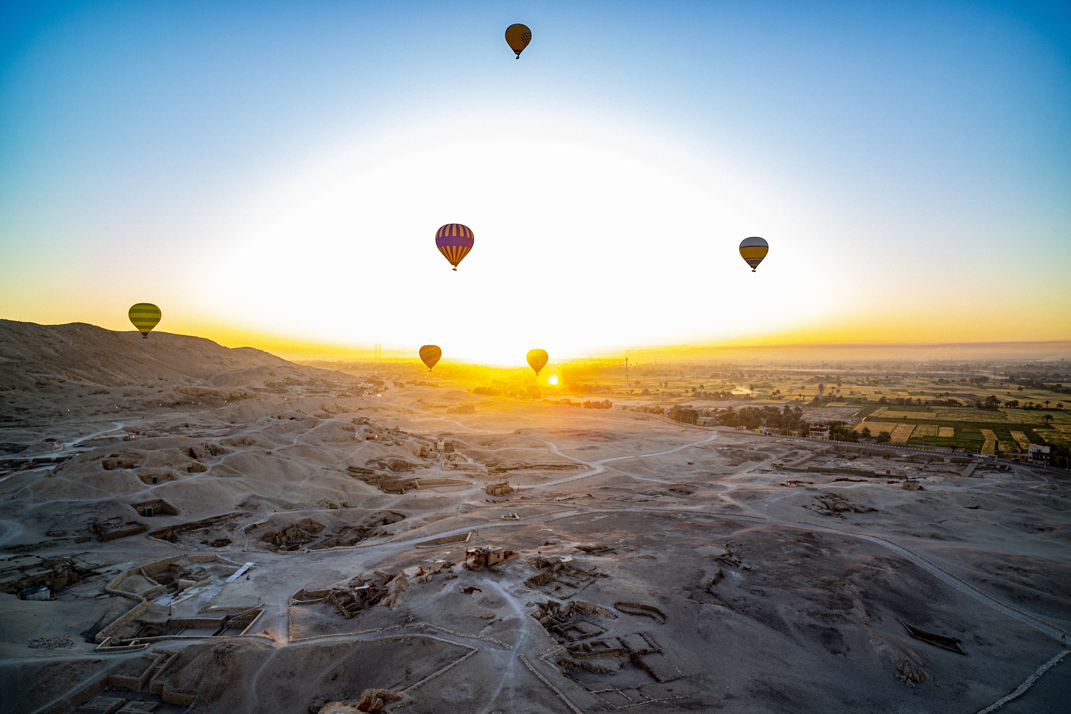 Luchtballonnen zweven boven tempelruïnes en groene velden bij Luxor langs de Nijl in Egypte.