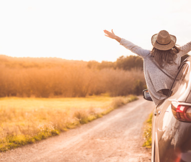 Vrouw hangt vrolijk uit een auto tijdens een roadtrip