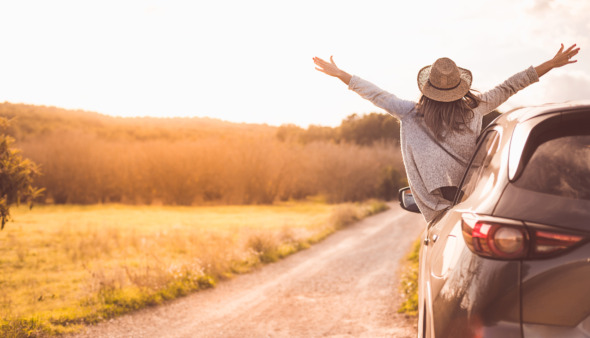 Vrouw hangt vrolijk uit een auto tijdens een roadtrip