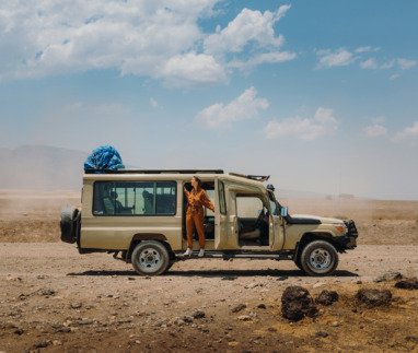 Vrouw in jumpsuit hangt uit een safari-jeep in Tanzania