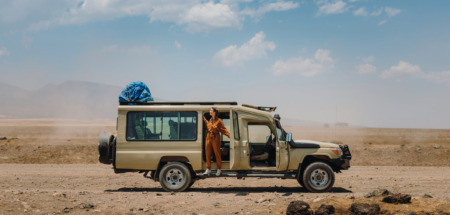 Vrouw in jumpsuit hangt uit een safari-jeep in Tanzania
