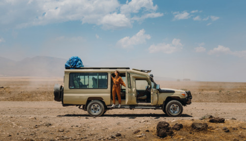 Vrouw in jumpsuit hangt uit een safari-jeep in Tanzania