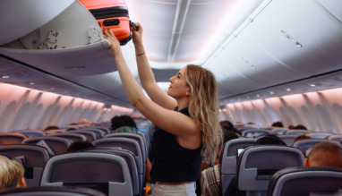 Vrouwelijke passagier bergt haar koffer weg in de bagagebak in het vliegtuig