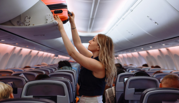 Vrouwelijke passagier bergt haar koffer weg in de bagagebak in het vliegtuig