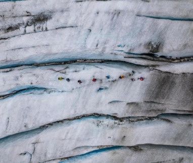 Groep wandelaars loopt aangelijnd over een gletsjer met diepe ijsspleten.