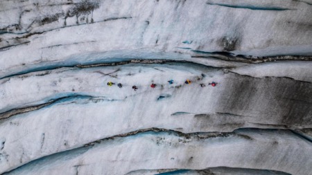 Groep wandelaars loopt aangelijnd over een gletsjer met diepe ijsspleten.