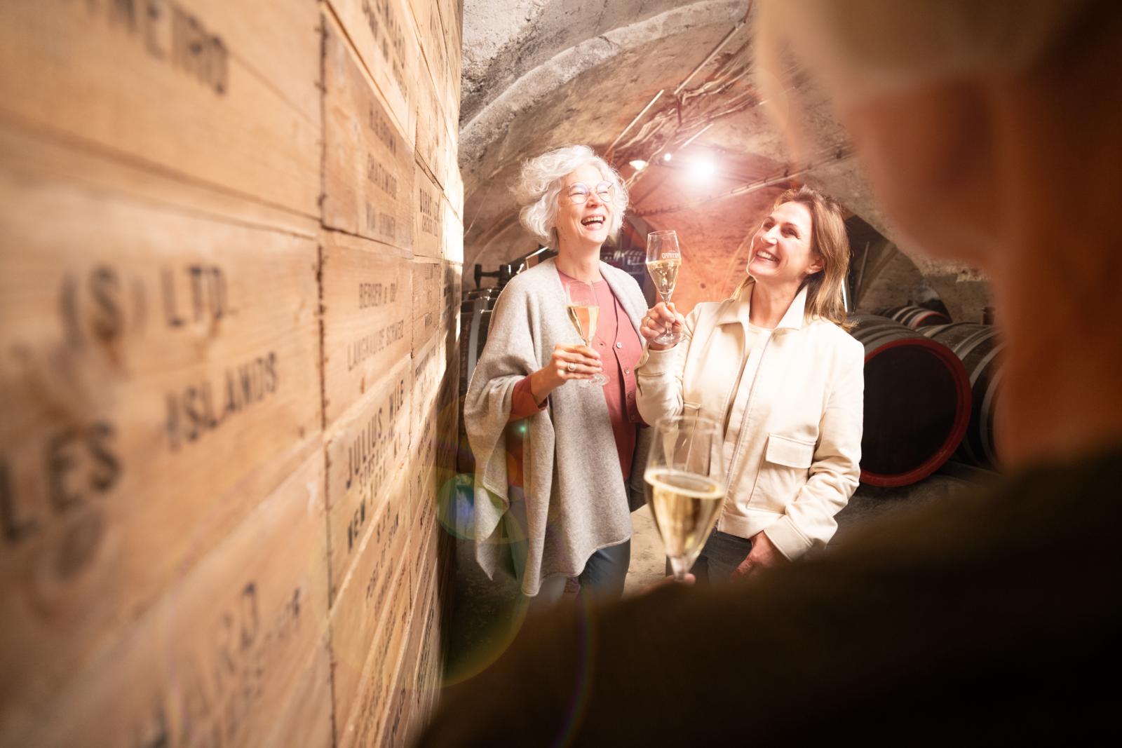 Twee vrouwen proeven mousserende wijn in een sfeervolle ondergrondse wijnkelder in Duitsland.