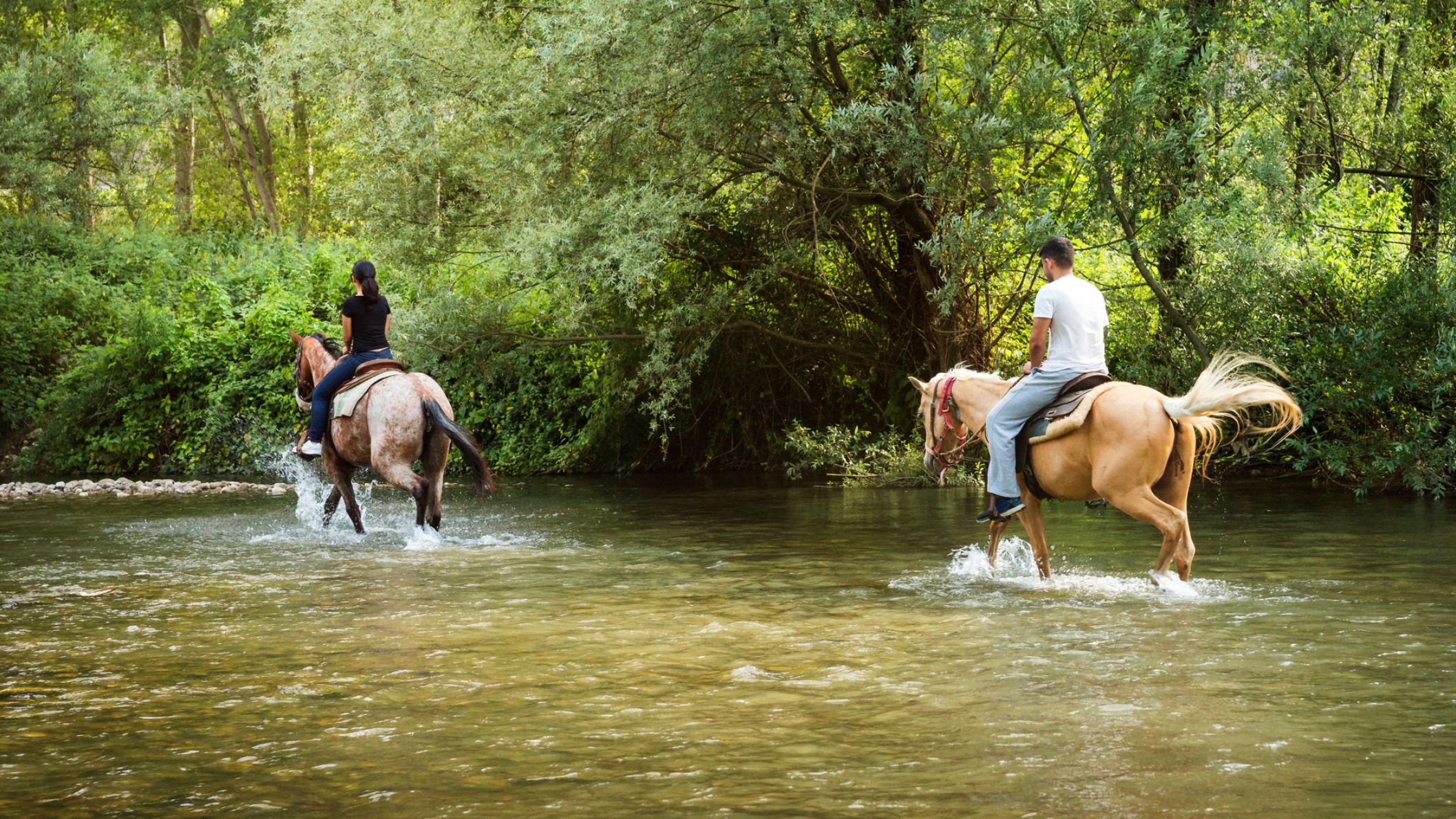 uiters te paard steken een rivier over in het groene landschap van de Abruzzen in Italië.