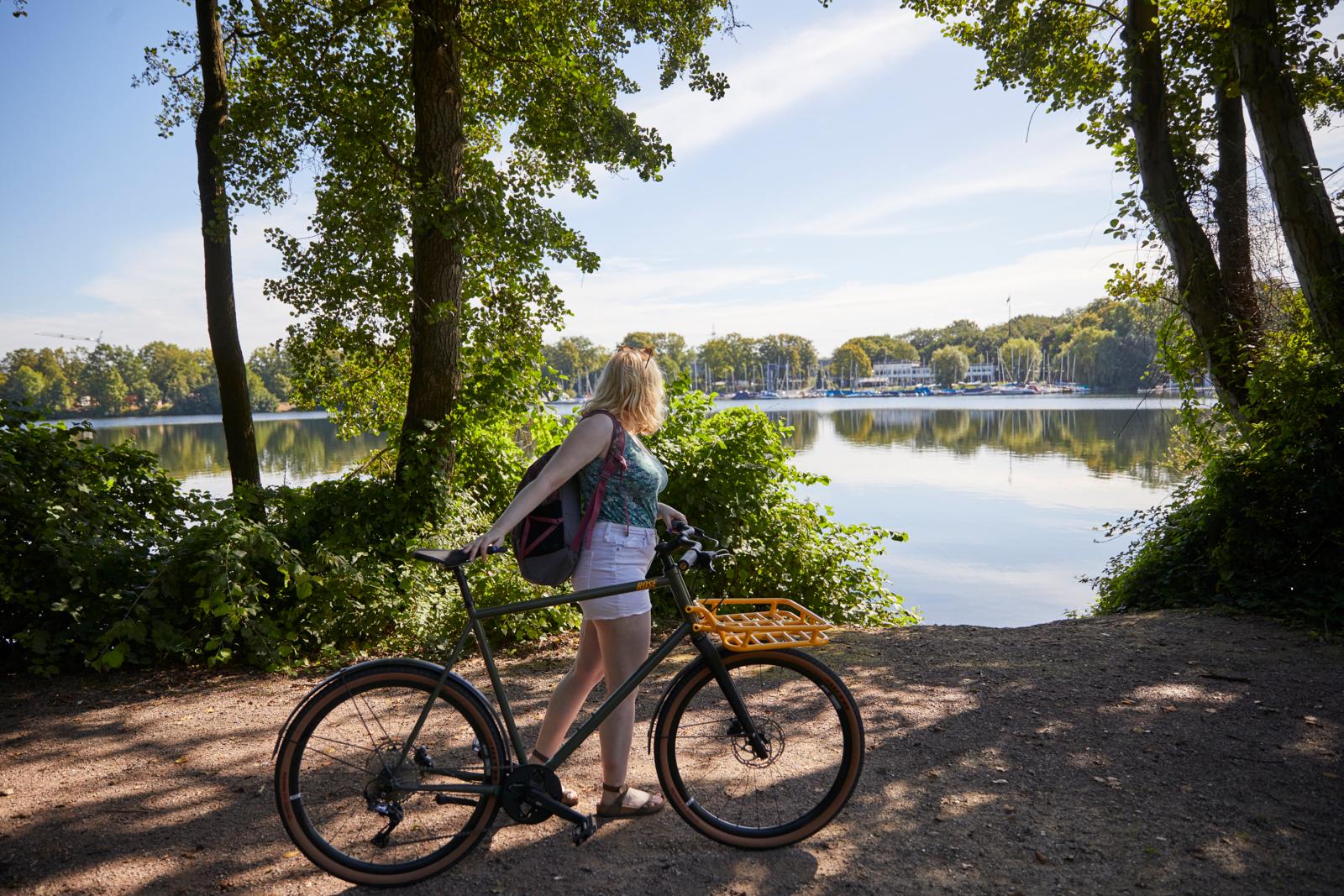 Vrouw met fiets aan de Sechs-Seen-Platte in Duisburg met uitzicht over het water en de jachthaven.