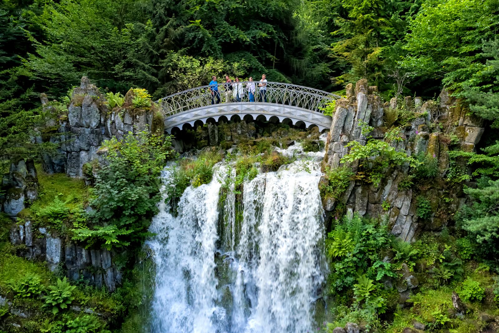 Bezoekers staan op een brug boven een waterval tijdens de Wasserspiele in Bergpark Wilhelmshöhe in Duitsland.