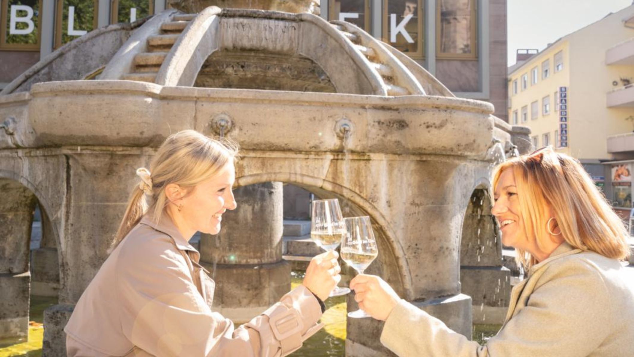 Twee vrouwen proosten met witte wijn bij een fontein in Worms, Duitsland tijdens een wijnfestival.