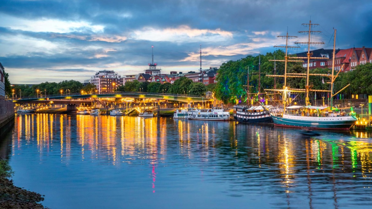Verlichte kade met historische schepen langs de Weser bij de Schlachte in Bremen bij avond.
