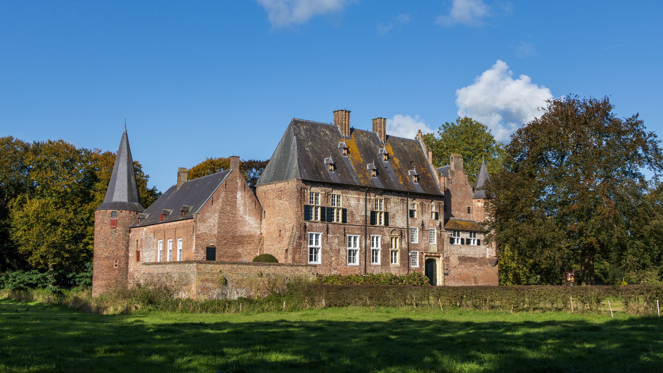 Een indrukwekkend middeleeuws bakstenen kasteel met torens onder een blauwe lucht met wolken.