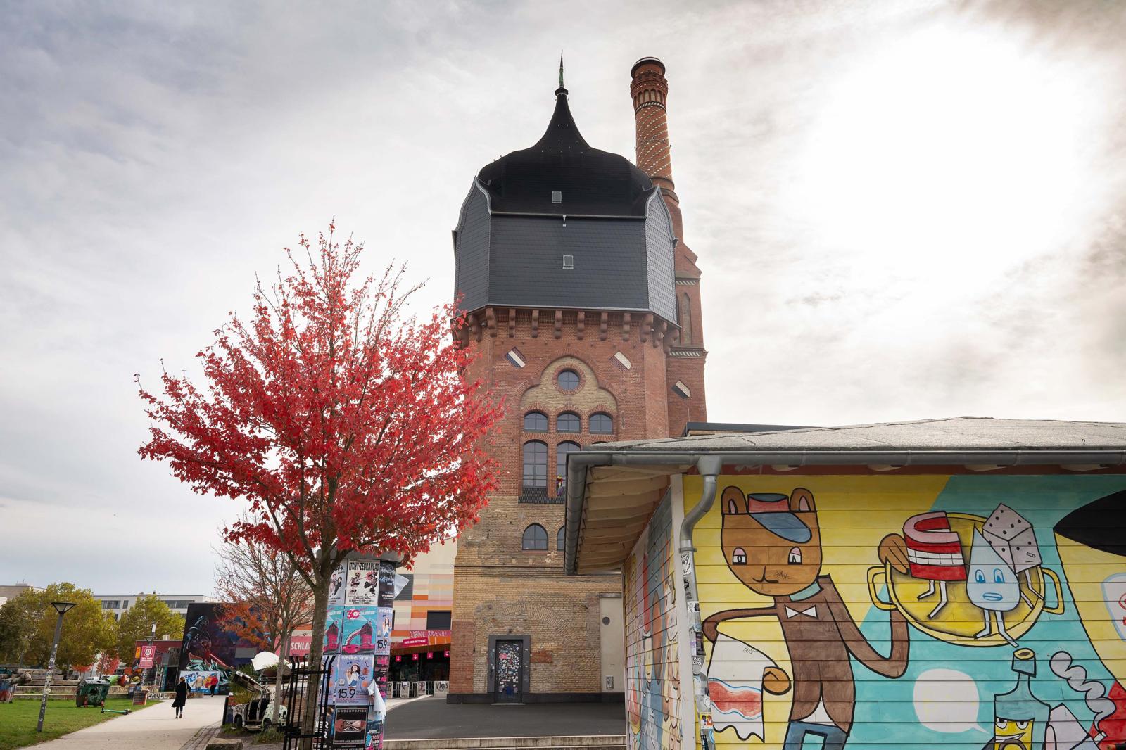 Een historisch bakstenen gebouw met watertoren en kleurrijke graffiti in het cultuurpark Schlachthof Wiesbaden.