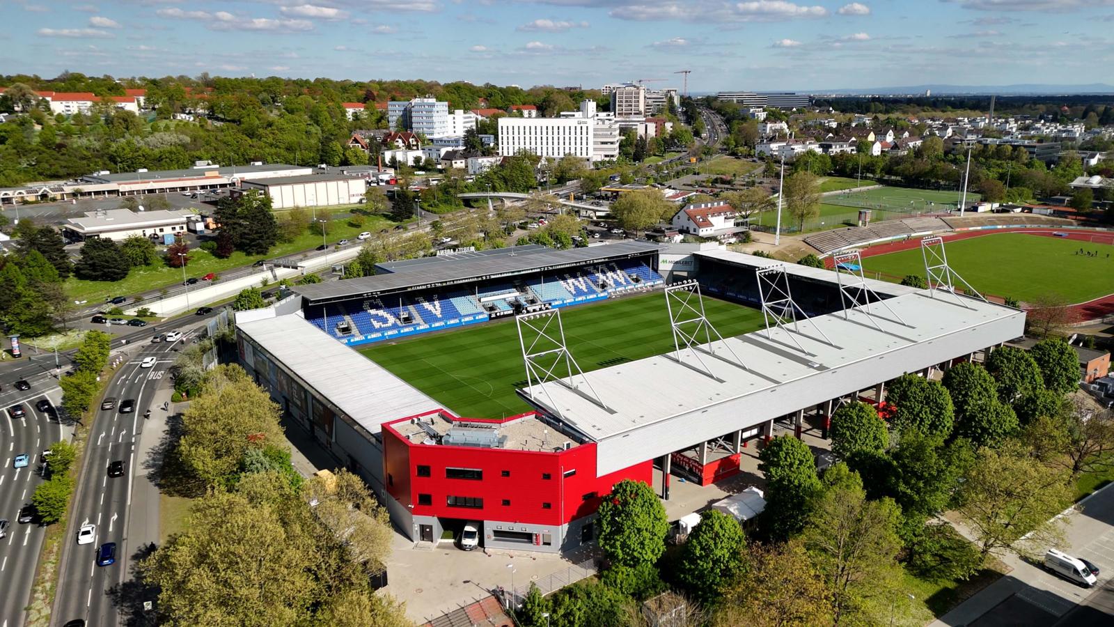 Een bovenaanzicht van het moderne BRITA-Arena voetbalstadion met blauwe tribunes en een groen veld in Wiesbaden.