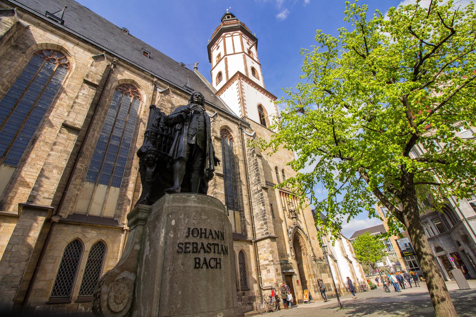 Bronzen monument van componist Johann Sebastian Bach in Leipzig met de Thomaskirche op de achtergrond.