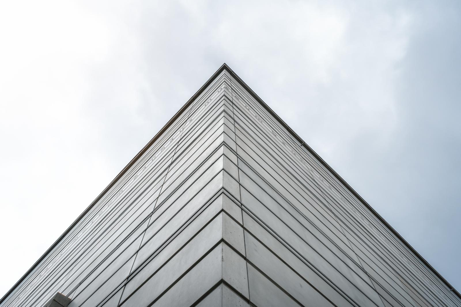 Detailopname van de minimalistische, grijze betongevel van het Bauhaus-Museum Weimar tegen een bewolkte lucht.