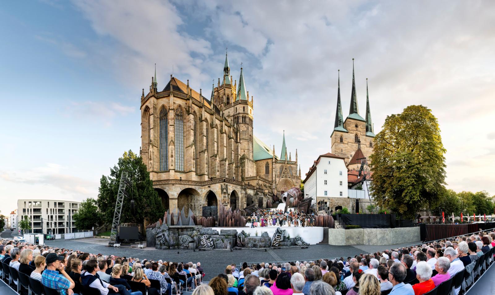 Een groot publiek kijkt naar een theatervoorstelling op de trappen van de verlichte Dom van Erfurt.
