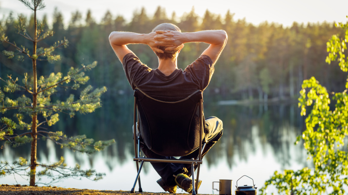 Man geniet in campingstoel van het uitzicht over een meer in een bos in Finland