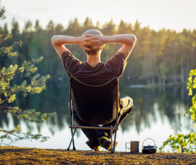 Man geniet in campingstoel van het uitzicht over een meer in een bos in Finland