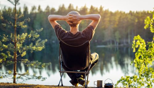 Man geniet in campingstoel van het uitzicht over een meer in een bos in Finland