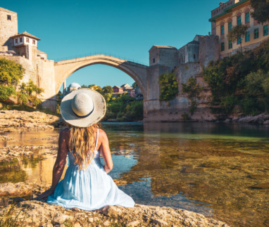 Vrouw in witte jurk kijkt uit over de oude brug in Mostar, Bosnië