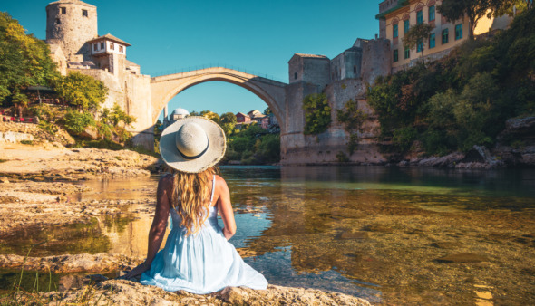 Vrouw in witte jurk kijkt uit over de oude brug in Mostar, Bosnië