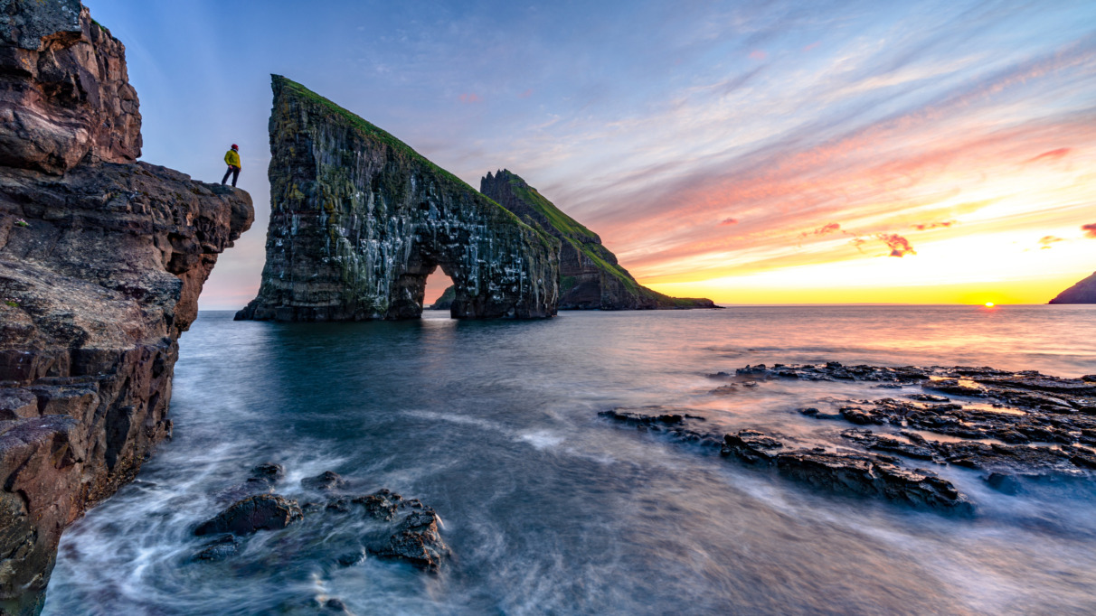 Hiker kijkt naar zonsondergang bij Drangarnir op de Faeroer in Denemarken