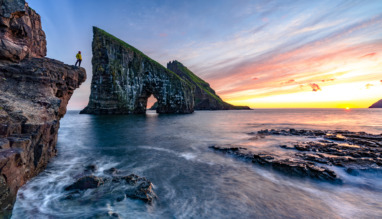 Hiker kijkt naar zonsondergang bij Drangarnir op de Faeroer in Denemarken
