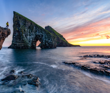 Hiker kijkt naar zonsondergang bij Drangarnir op de Faeroer in Denemarken