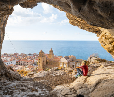 Persoon in grot boven Cefalù, Sicilië, kijkt uit over stad en zee