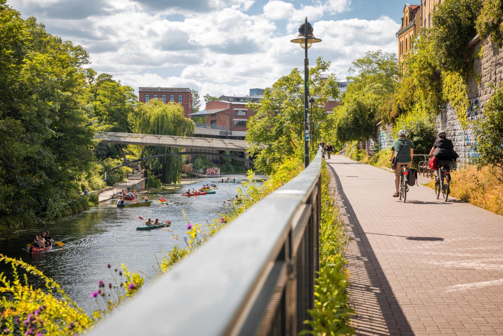 Mensen varen in kano's op het water terwijl fietsers over het pad langs het Karl-Heine-Kanal in Leipzig rijden.