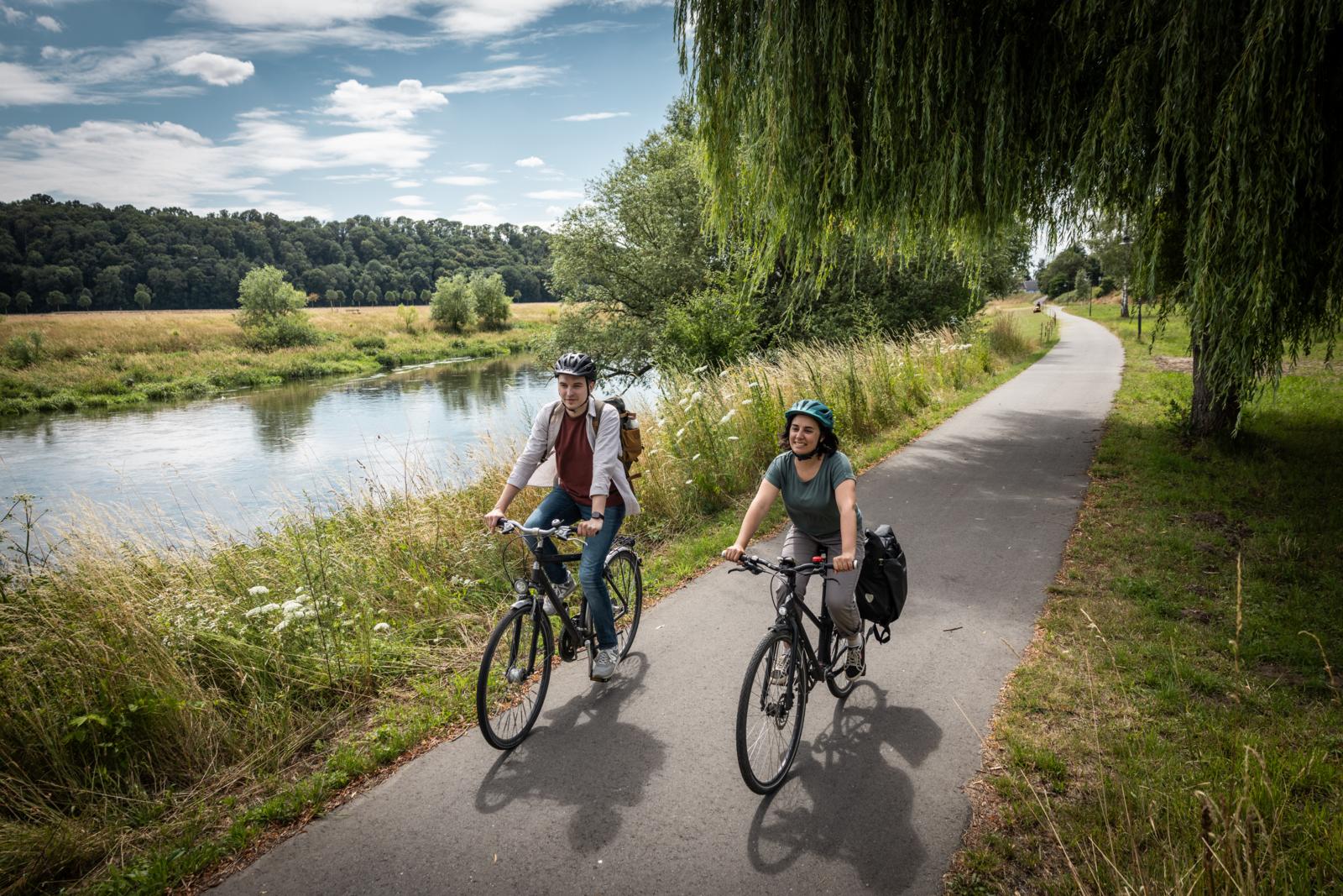 Twee fietsers op een geasfalteerd fietspad door een groen landschap langs de oever van de Mulde.
