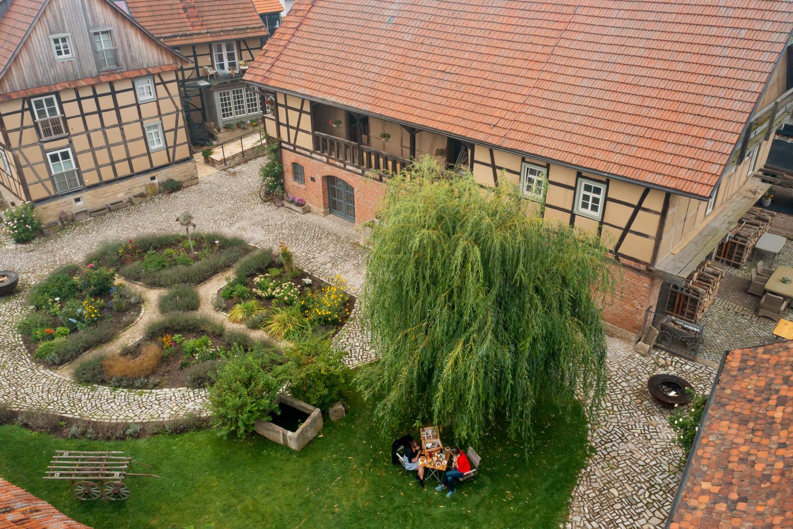 Bovenaanzicht van een groene binnentuin met vakwerkhuizen en gasten die buiten dineren bij restaurant Magda.