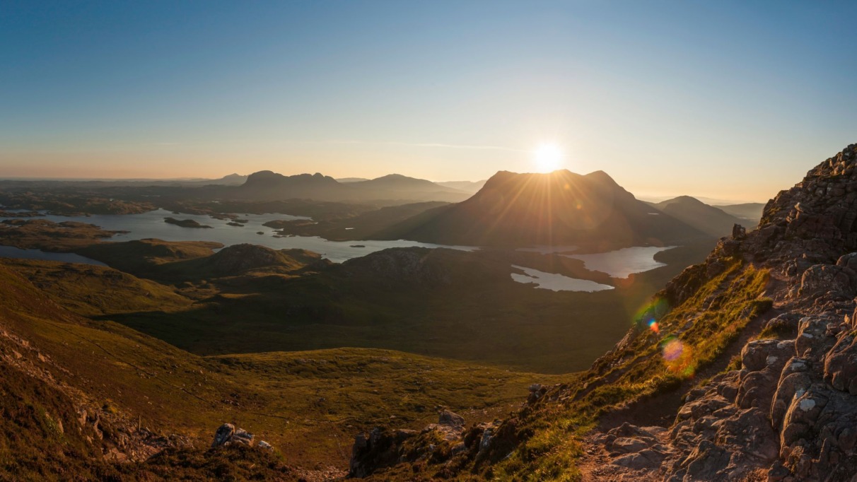 Panoramisch uitzicht vanaf een bergpad op een zonovergoten landschap met lochs in Sutherland.