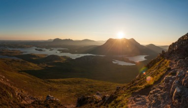 Panoramisch uitzicht vanaf een bergpad op een zonovergoten landschap met lochs in Sutherland.