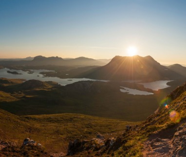 Panoramisch uitzicht vanaf een bergpad op een zonovergoten landschap met lochs in Sutherland.