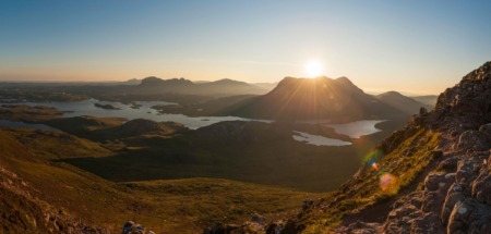 Panoramisch uitzicht vanaf een bergpad op een zonovergoten landschap met lochs in Sutherland.