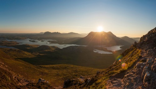 Panoramisch uitzicht vanaf een bergpad op een zonovergoten landschap met lochs in Sutherland.