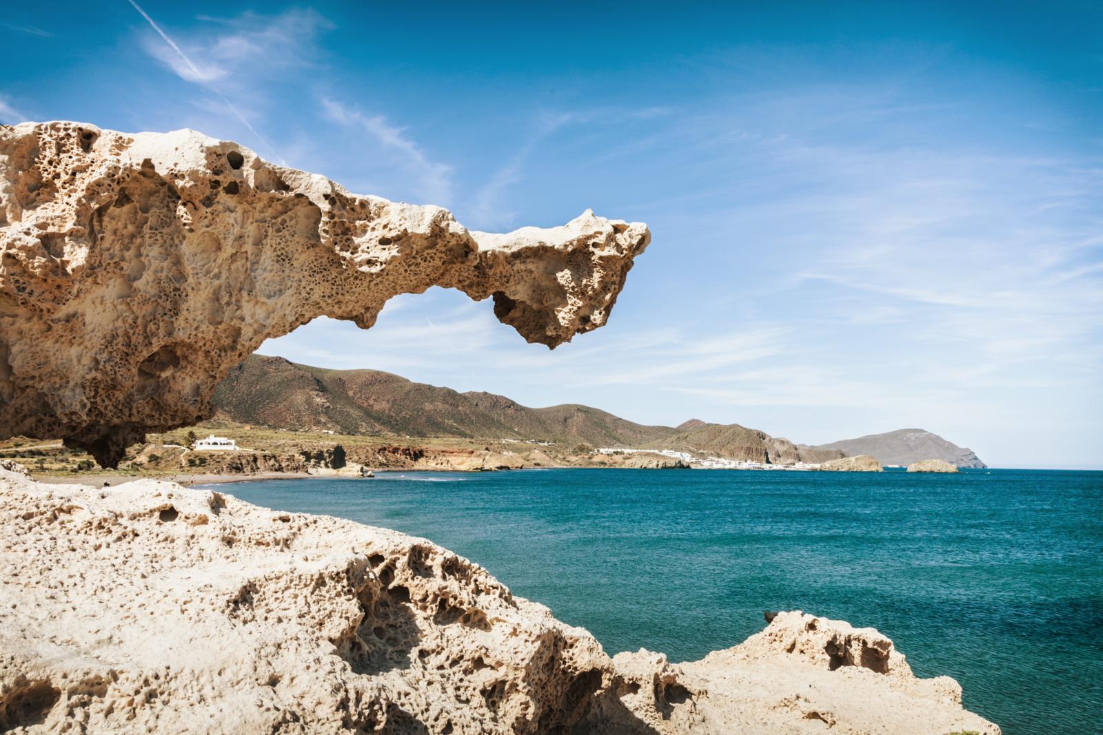 Een indrukwekkende, door erosie gevormde rotsformatie op de voorgrond met uitzicht op de diepblauwe Middellandse Zee en de dorre bergen van Andalusië.