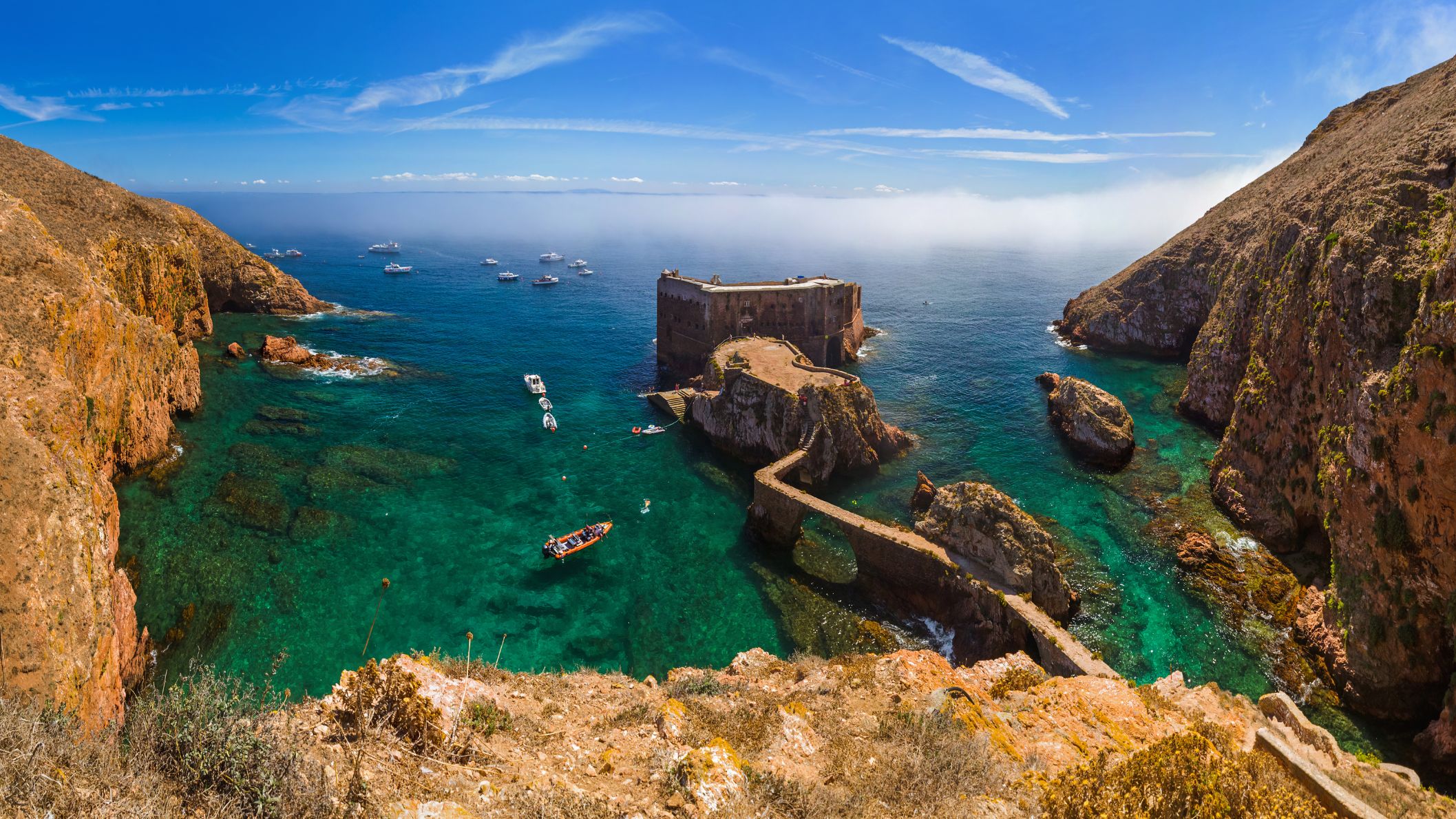 Een indrukwekkend stenen fort op een klein eiland in de Atlantische Oceaan, verbonden met het hoofdeiland Berlenga Grande door een smalle stenen boogbrug over kristalhelder turquoise water.