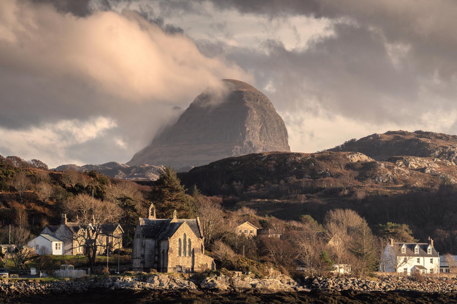 Historisch stenen kerkje aan de kust van Lochinver met de berg Suilven in de wolken.