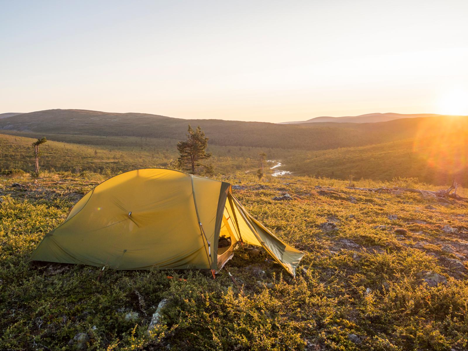 Een gele tent op een heuvel in Nationaal Park Urho Kekkonen tijdens een goudgele zonsondergang over het uitgestrekte Finse toendralandschap.