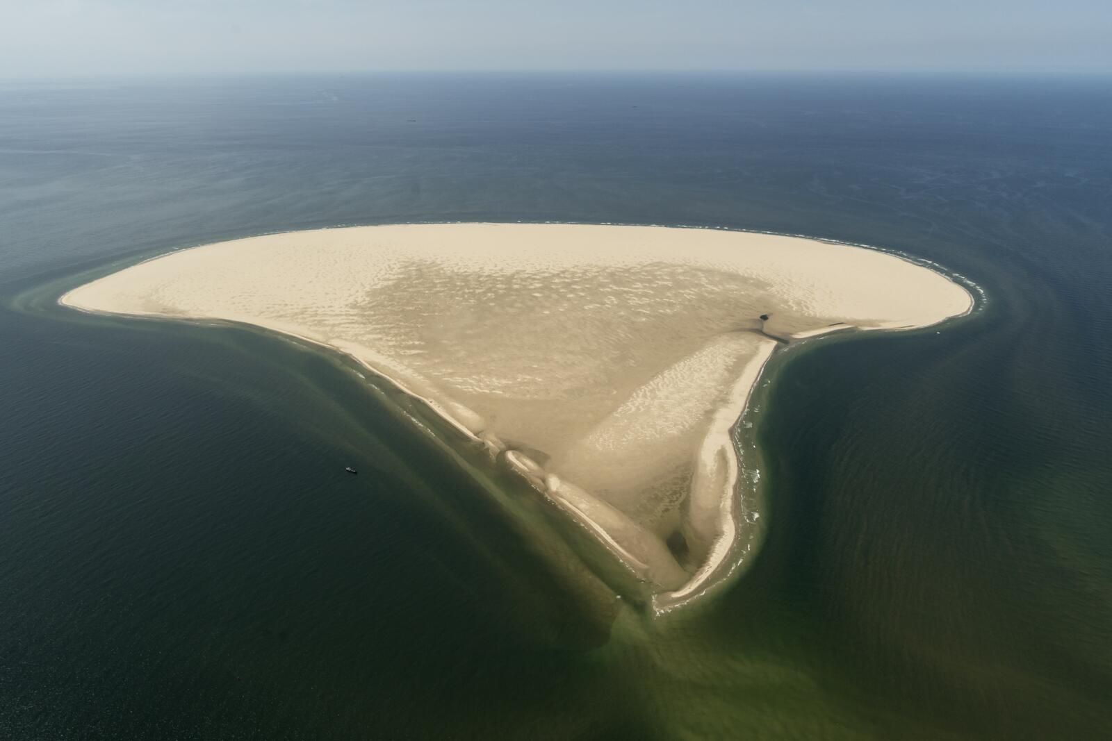 Luchtfoto van de Razende Bol, een uitgestrekte goudgele zandplaat omringd door diepblauw zeewater.