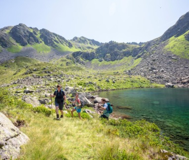 Drie bergwandelaars met wandelstokken passeren een turquoise bergmeer in het ruige landschap van Oostenrijk.