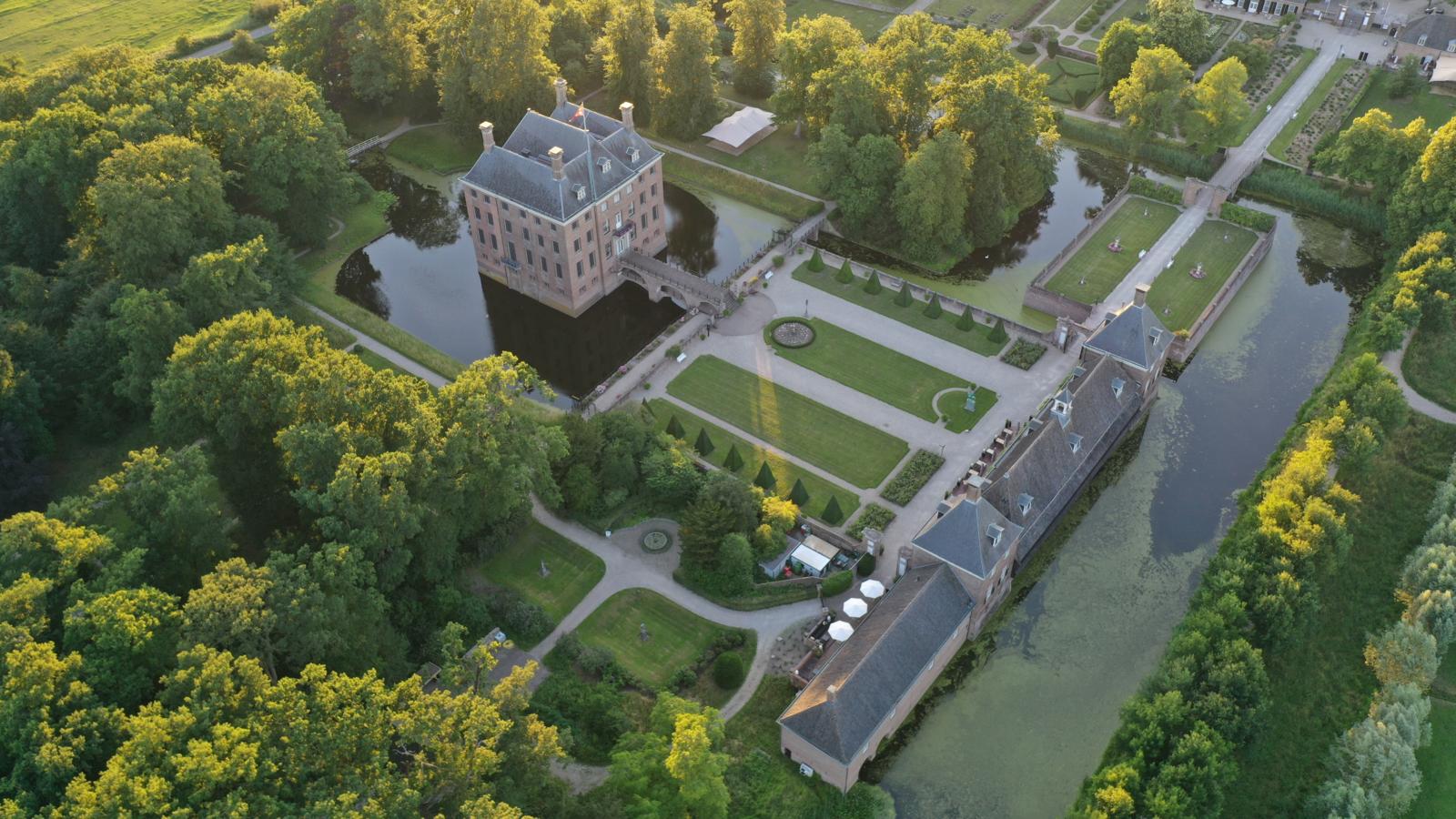 Luchtfoto van het omgrachte Kasteel Amerongen en de strakke kasteeltuinen in het zachte avondlicht