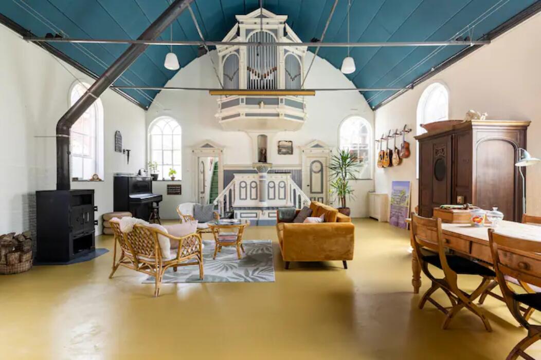 Interieur van een voormalig kerkje met een blauw gewelfd plafond, een kerkorgel en een gezellige woonkamerinrichting.
