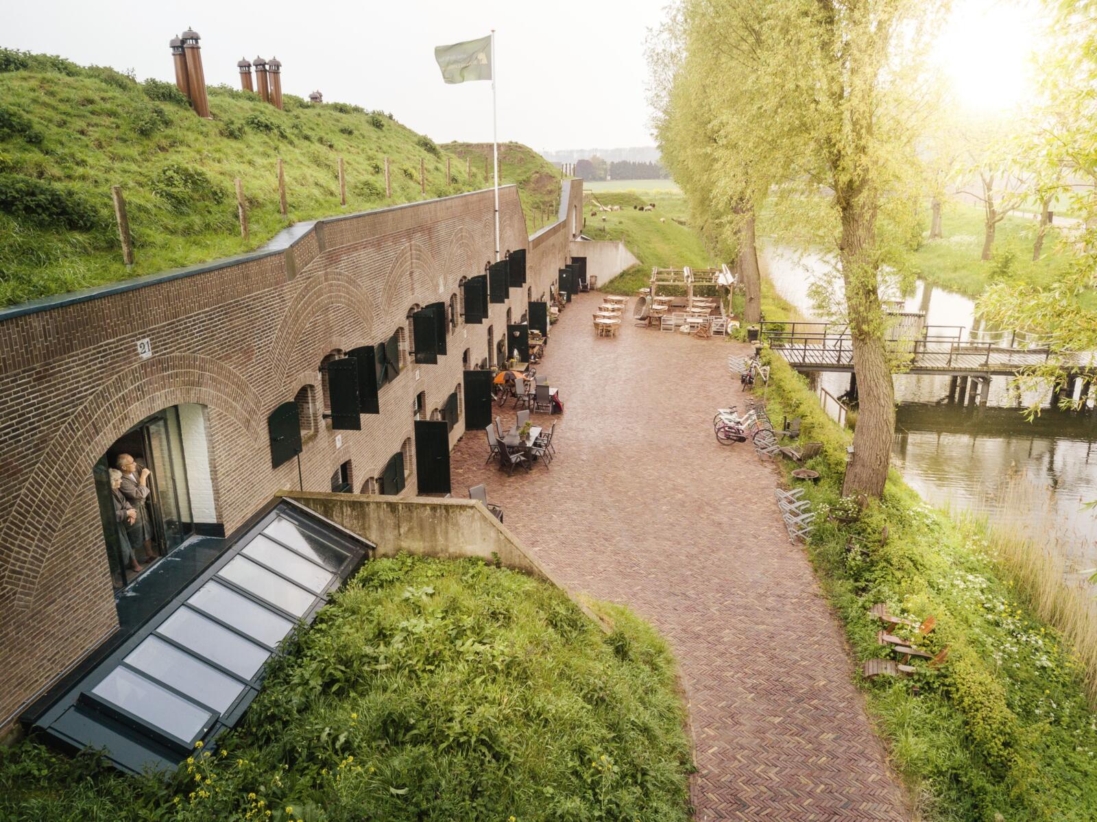 Bovenaanzicht van de bakstenen kazematten van Fort Bakkerskil met terras en bruggetje over de gracht bij zonsondergang.